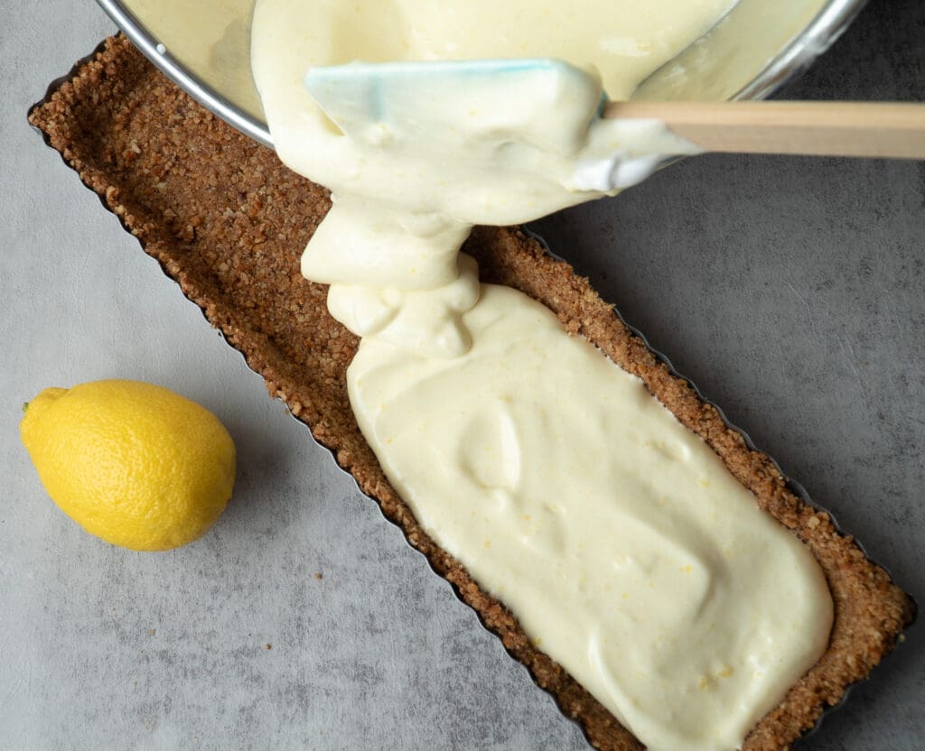 Using a spatula to guide lemon filling into a rectangular shaped crust.
