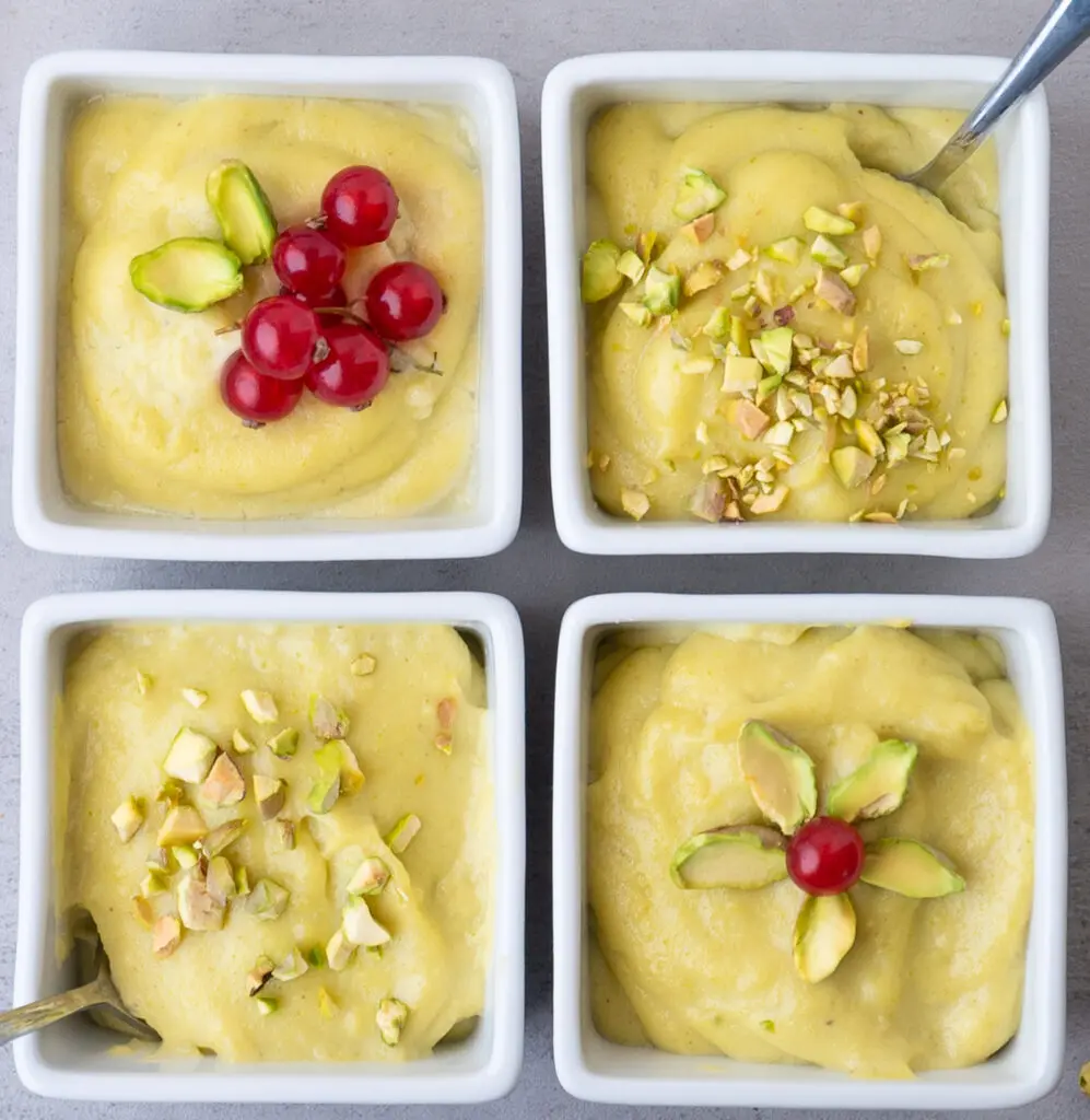 Four square dessert cups filled with pistachio pudding, crushed pistachio nuts and two have red currant berries on them.