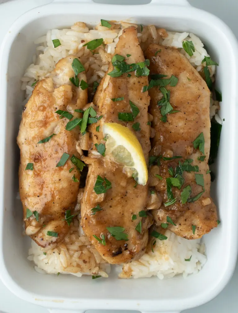 three strips of garlic lemon chicken in a small white dish on a bed of rice with a small lemon slice on tip.