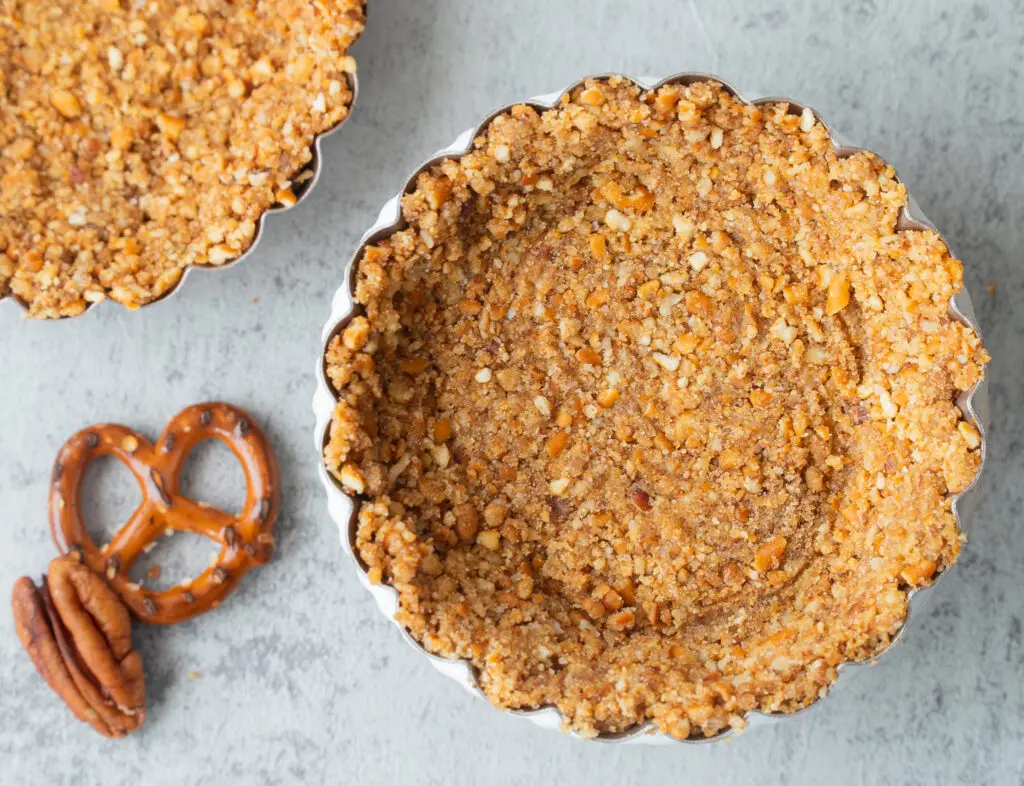 Mini baked pretzel pecan pie crust with pretzel and pecan garnish on the side.