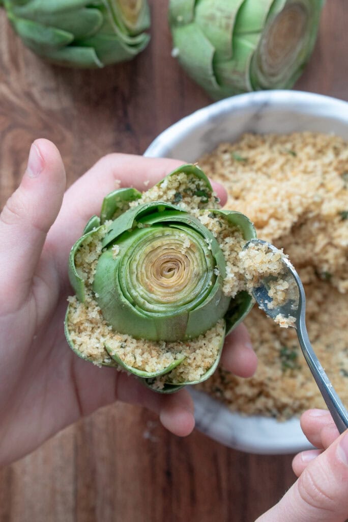 child's hands holding an artichoke and it with a spoon