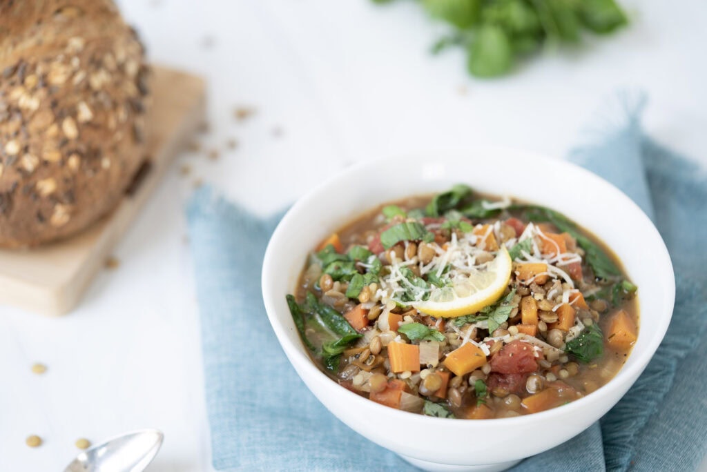 3/4 shot of a lentil soup with crusty bread in the background and blue napkin underneath