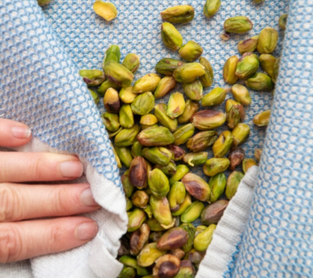 Hand pictured next to pistachios on a dish towel