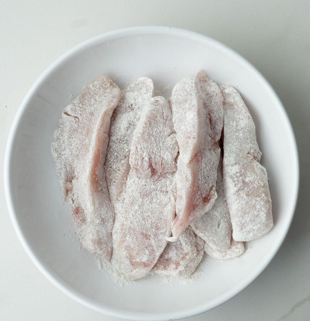 White plate with raw chicken strips dredged in flour