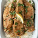 three strips of garlic lemon chicken in a small white dish on a bed of rice with a small lemon slice on tip.