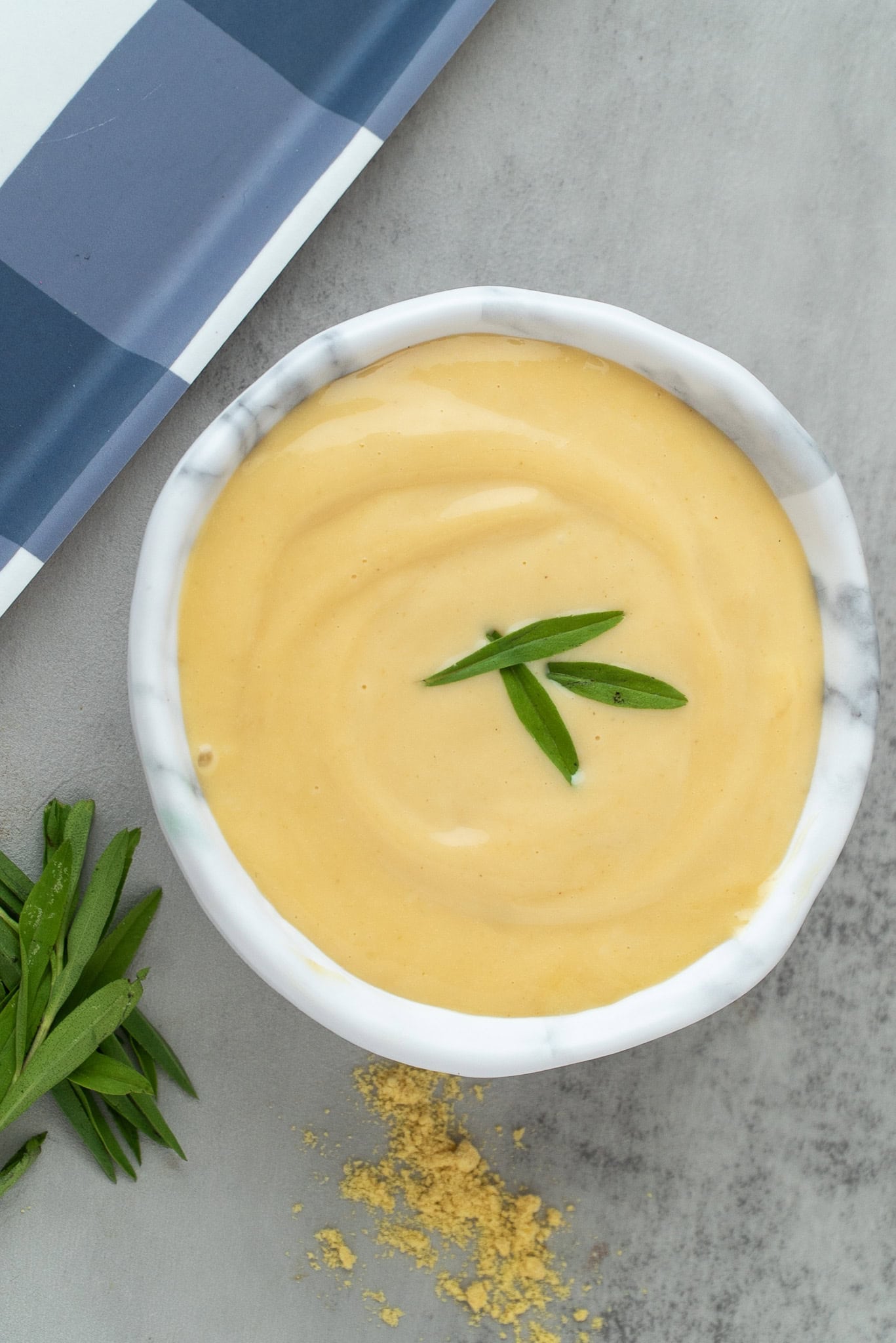 Old Fashioned Creamy Mustard Sauce in a small bowl with fresh tarragon leaves