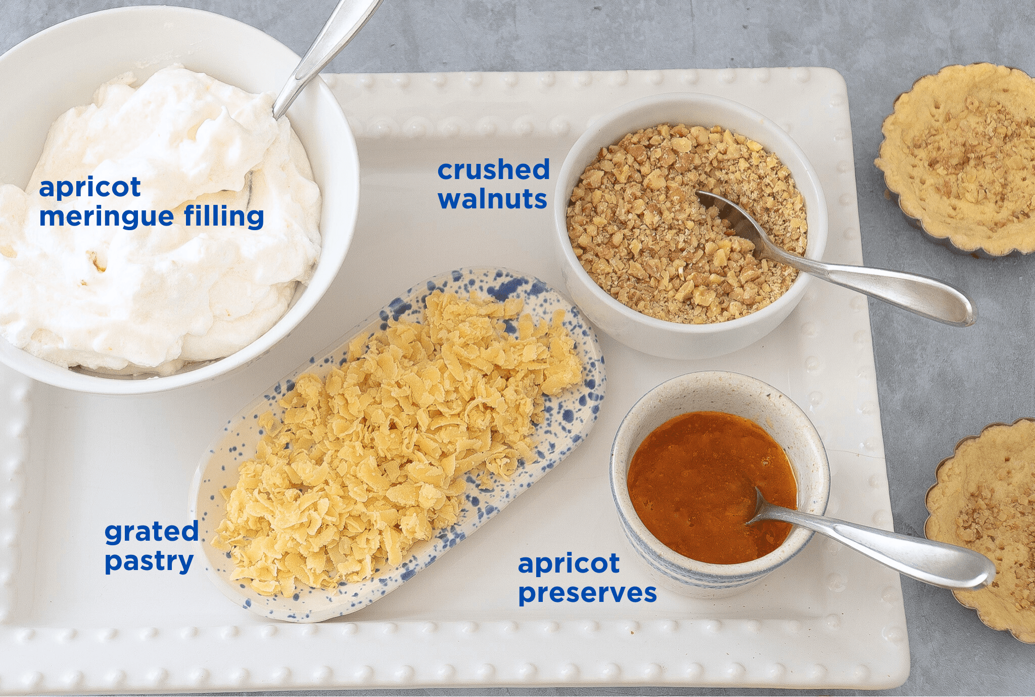 White Rectangular Plate with a bowl of meringue filling, grated pastry, apricot preserves and crushed walnuts to fill tart shells for Hungarian Apricot Ruffled Tarts Recipe