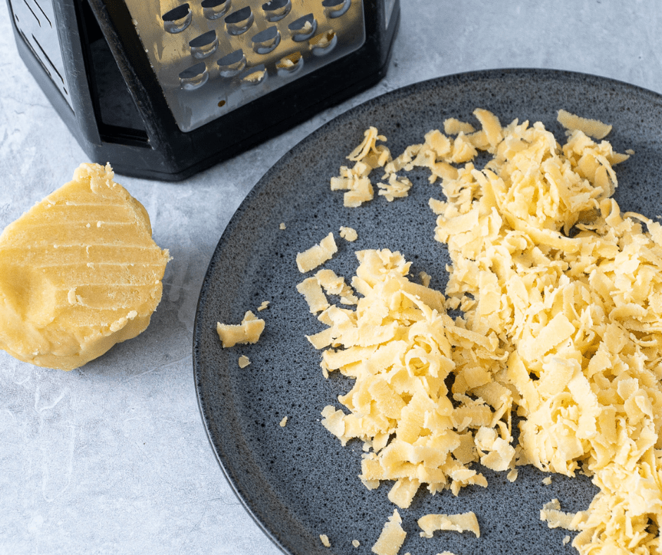 A dark gray plate with grated pastry dough on it, a ball of pastry dough beside it and a grater in the background | Hungarian Apricot Ruffled Tart Recipe