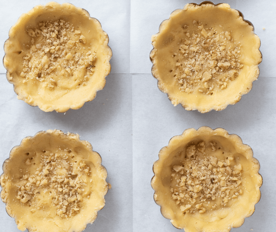 Four tart shells with pastry and nuts on a tray lined with parchment paper | Hungarian Apricot Ruffled Tarts Recipe