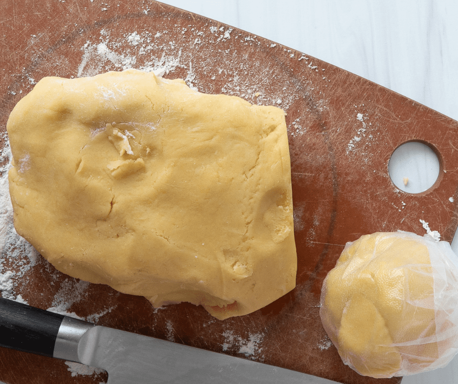 Pastry Dough on a wooden cutting board, One third of the dough is cut off and rolled into a ball with plastic wrap around it.