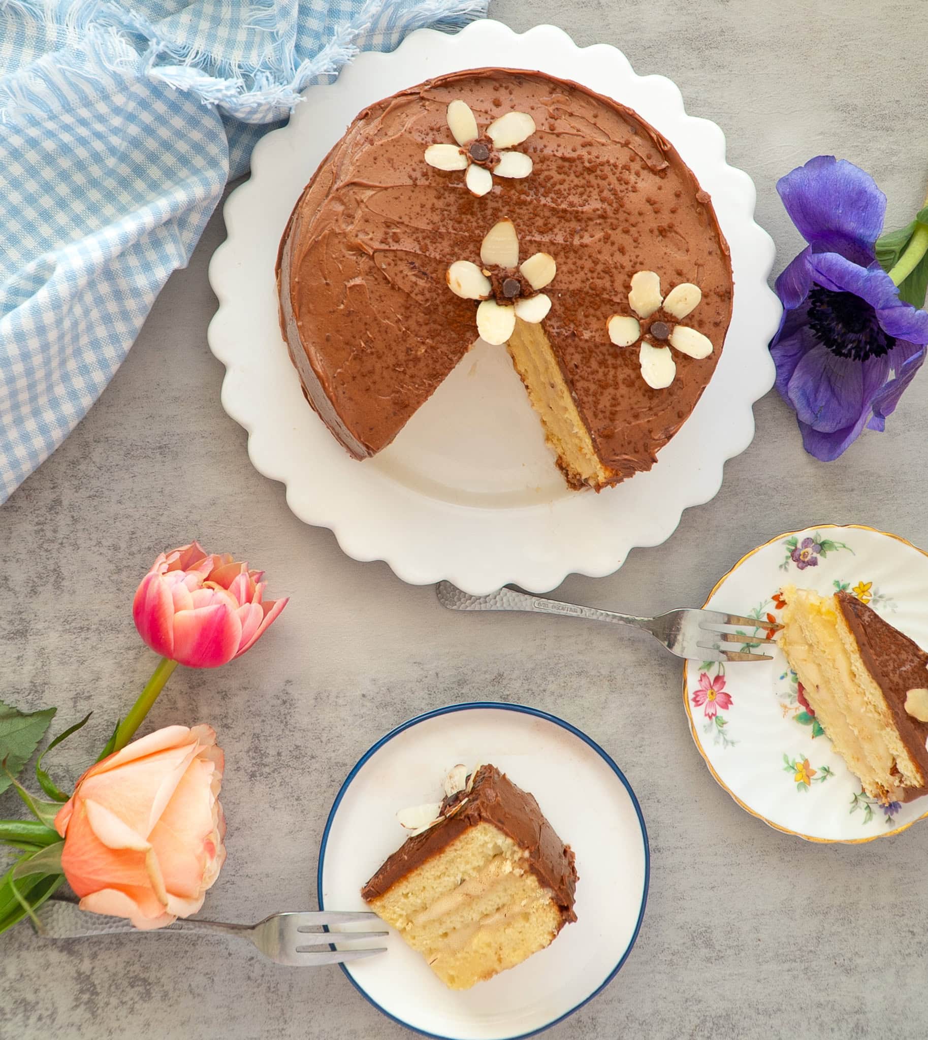 Decadent marzipan mocha cake with one slice cut, surrounded by spring flowers and two slices on a plate with mini forks.