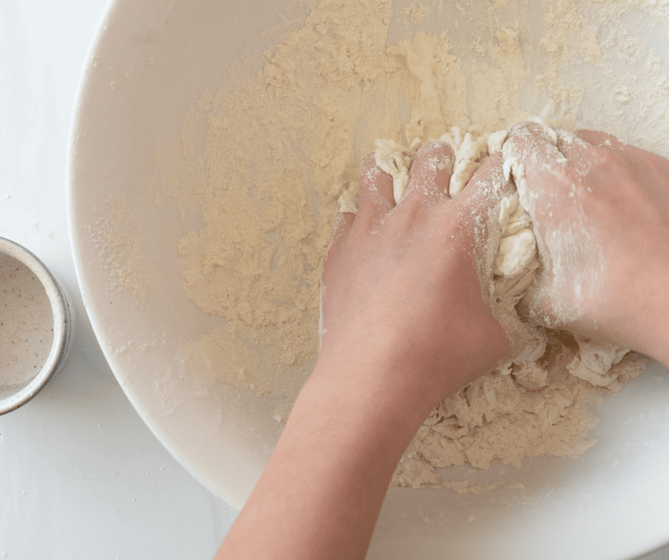 Two hands mixing homemade udon dough in a bowl.