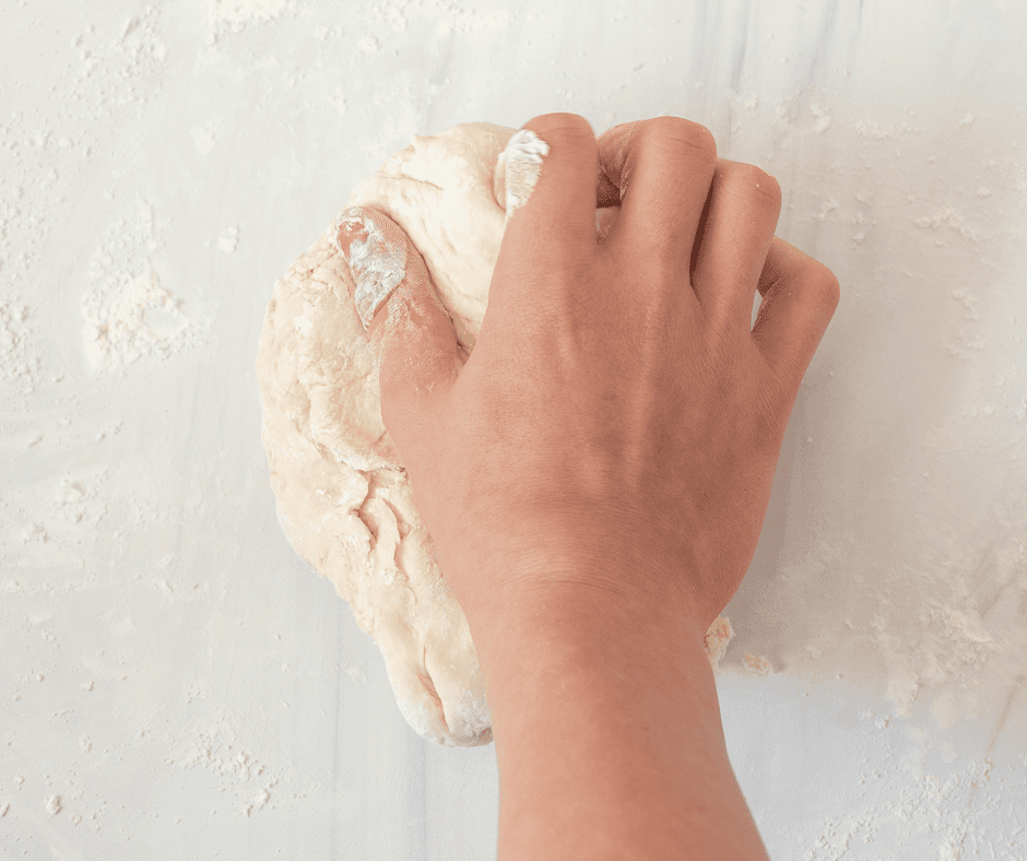 Kneading homemade udon dough with one hand on a floured surface.