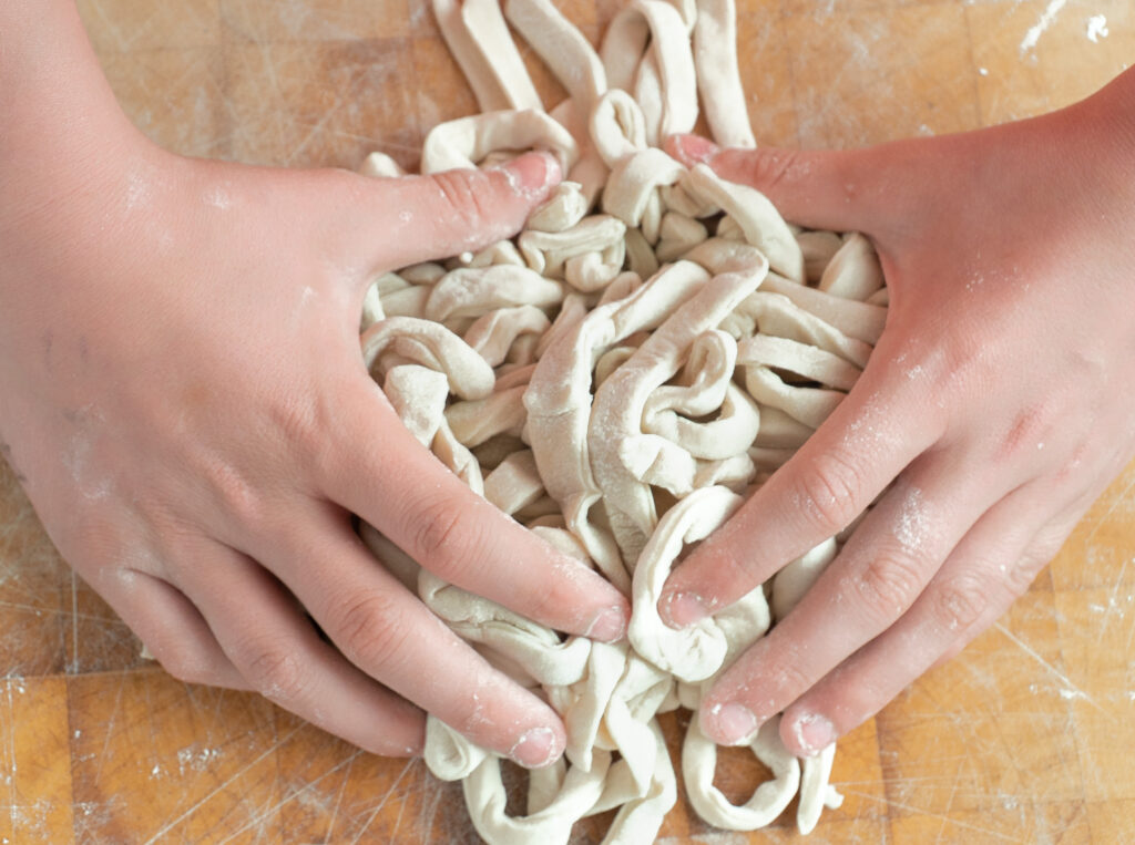 Step-by-step image showing how to make fresh udon noodles by rolling the dough on a floured surface