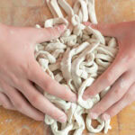 Step-by-step image showing how to make fresh udon noodles by rolling the dough on a floured surface