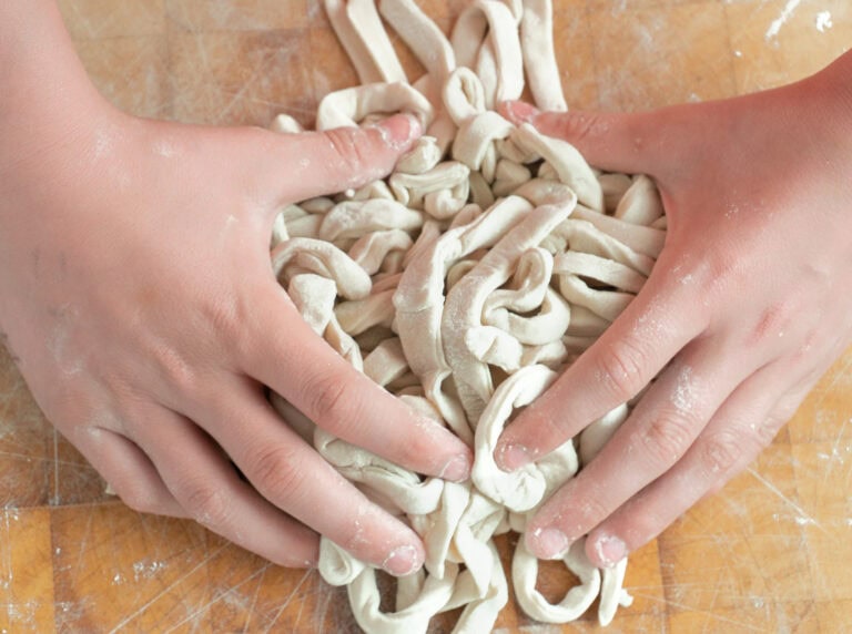 Step-by-step image showing how to make fresh udon noodles by rolling the dough on a floured surface
