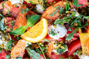 Colorful caprese salad with burrata, tomatoes, watermelon, oranges, and fresh herbs on a white plate