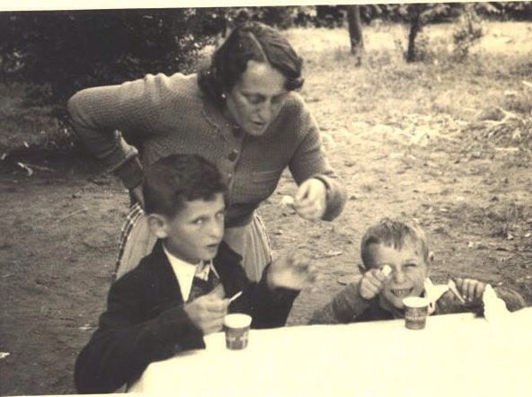 Black and white vintage photo of Maria in Budapest with her two sons, standing over them while they are enjoying a treat.