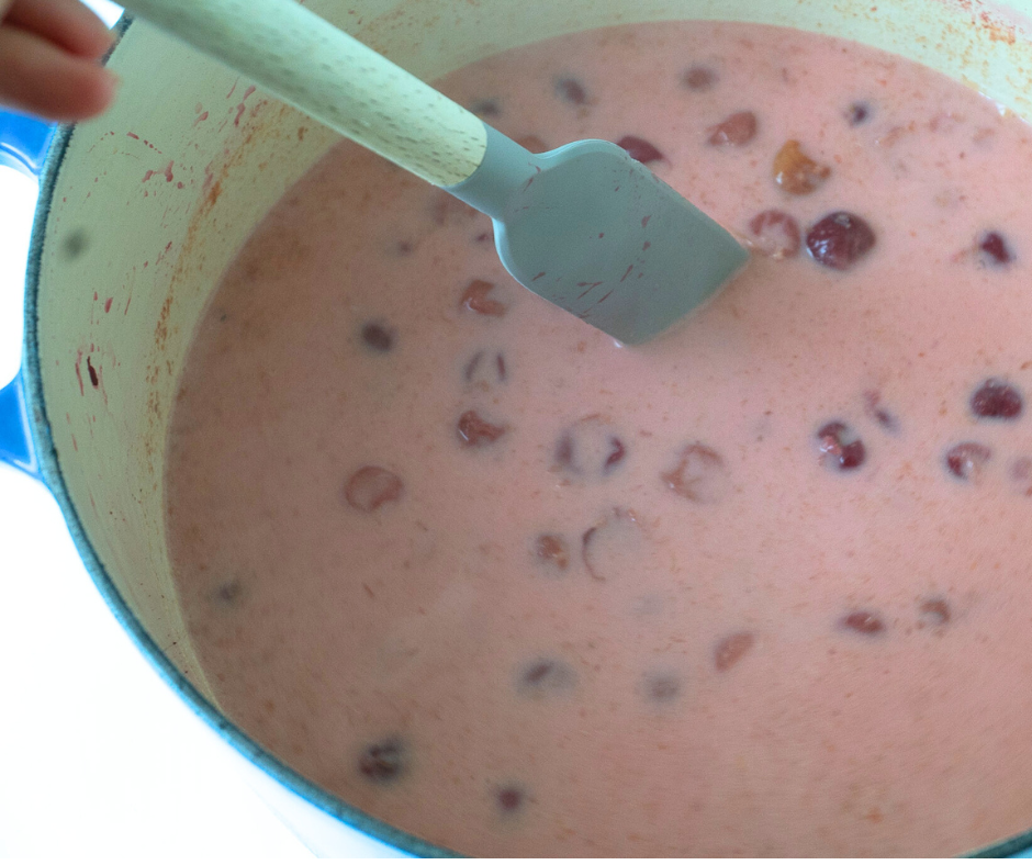 Spatula stirring simmering sour cherry soup on the stove in a large pot.