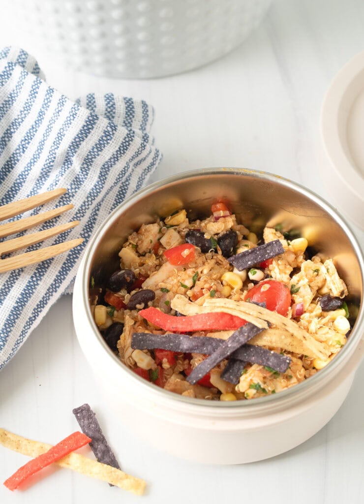 Close-up of a Tex-Mex Chicken Quinoa Bowl with colorful veggies, black beans, quinoa, and shredded chicken, styled with a striped napkin and bamboo fork.