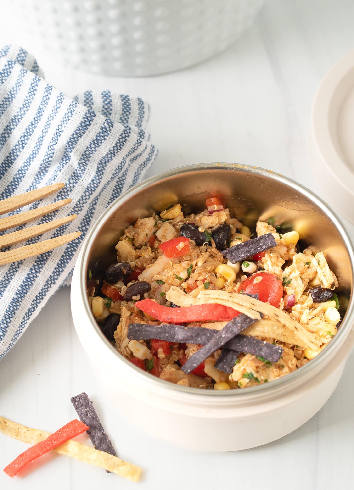 Close-up of a Tex-Mex Chicken Quinoa Bowl with colorful veggies, black beans, quinoa, and shredded chicken, styled with a striped napkin and bamboo fork.