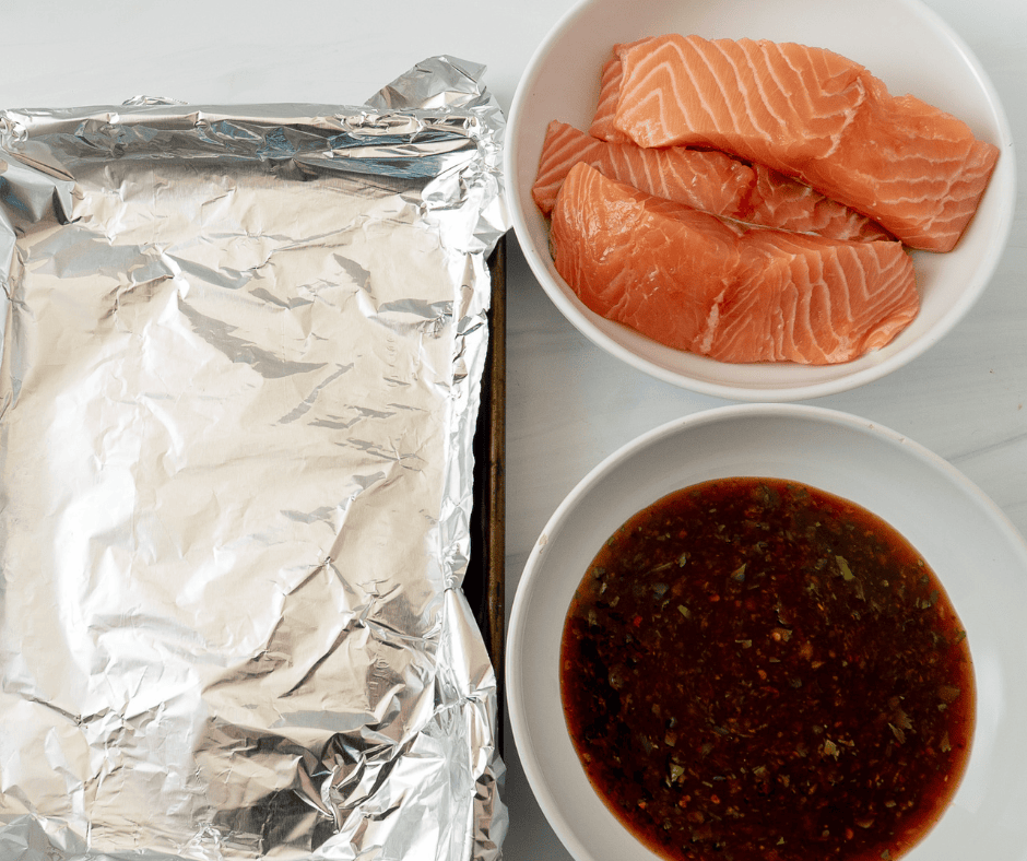 Salmon fillets in a foil-lined pan with separate bowl of marinade for Thai salmon rice bowls