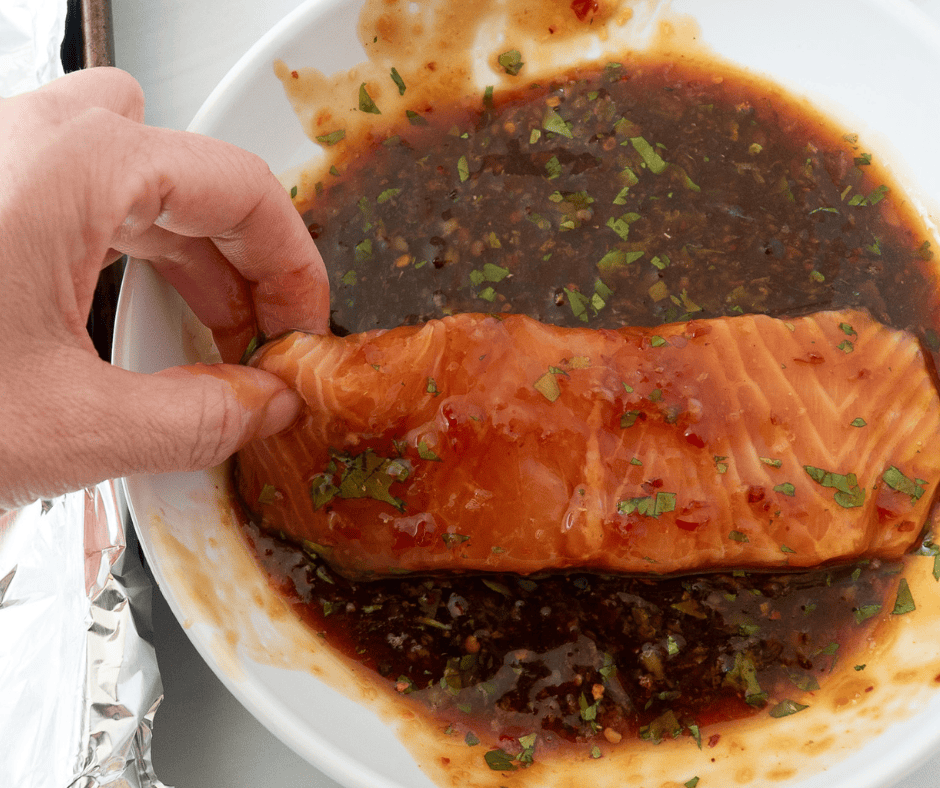 Hand turning salmon fillet in a bowl of marinade for Thai salmon rice bowls