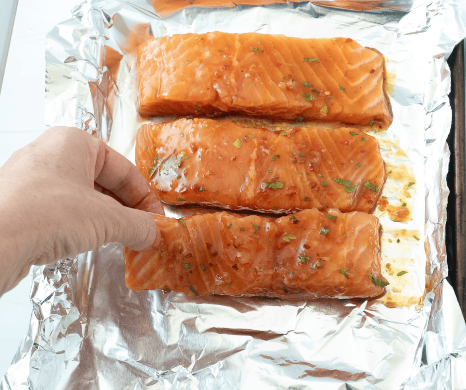 Hand placing salmon fillets on a foil-lined tray for Thai salmon rice bowls