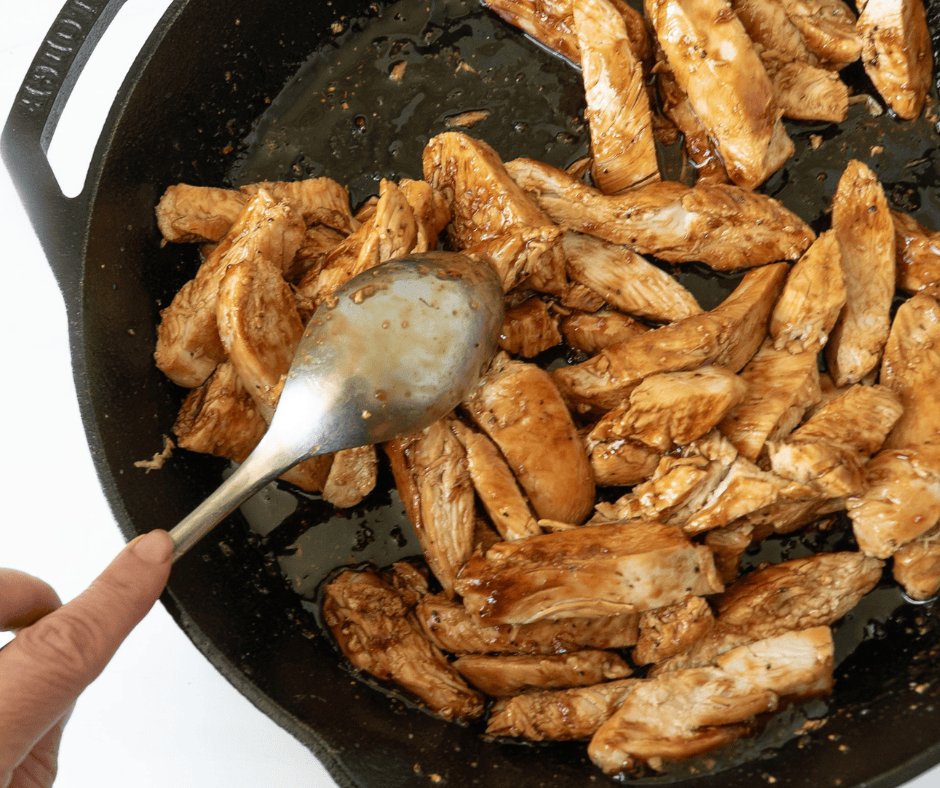 Glazing sliced cooked chicken in a pan with teriyaki sauce. 