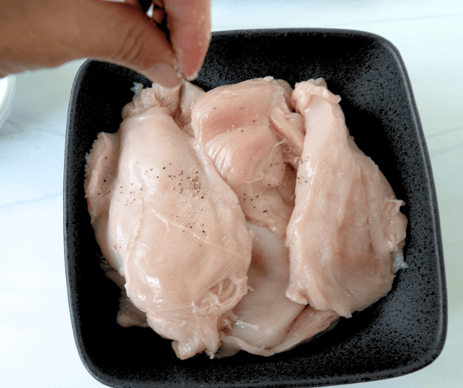 Sprinkling salt and pepper on trimmed, raw chicken for a Teriyaki Chicken Bento Box recipe 