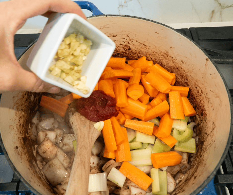 adding carrots, celery, garlic and tomato paste to onions for beef stew with her dumplings. 