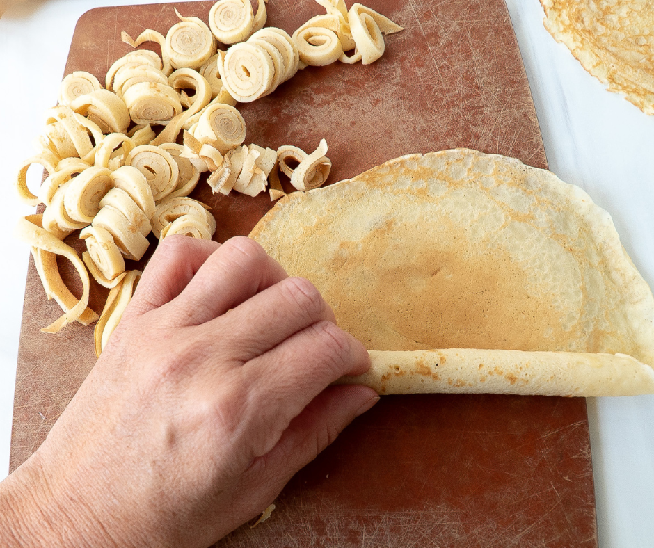 Cutting rolled up Austrian pancakes into noodles for Austrian Pancake Soup