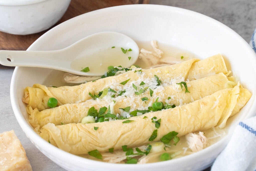 Close up of Scrippelle ‘Mbusse (Italian crepes in broth) three crepes in broth with garnishes.