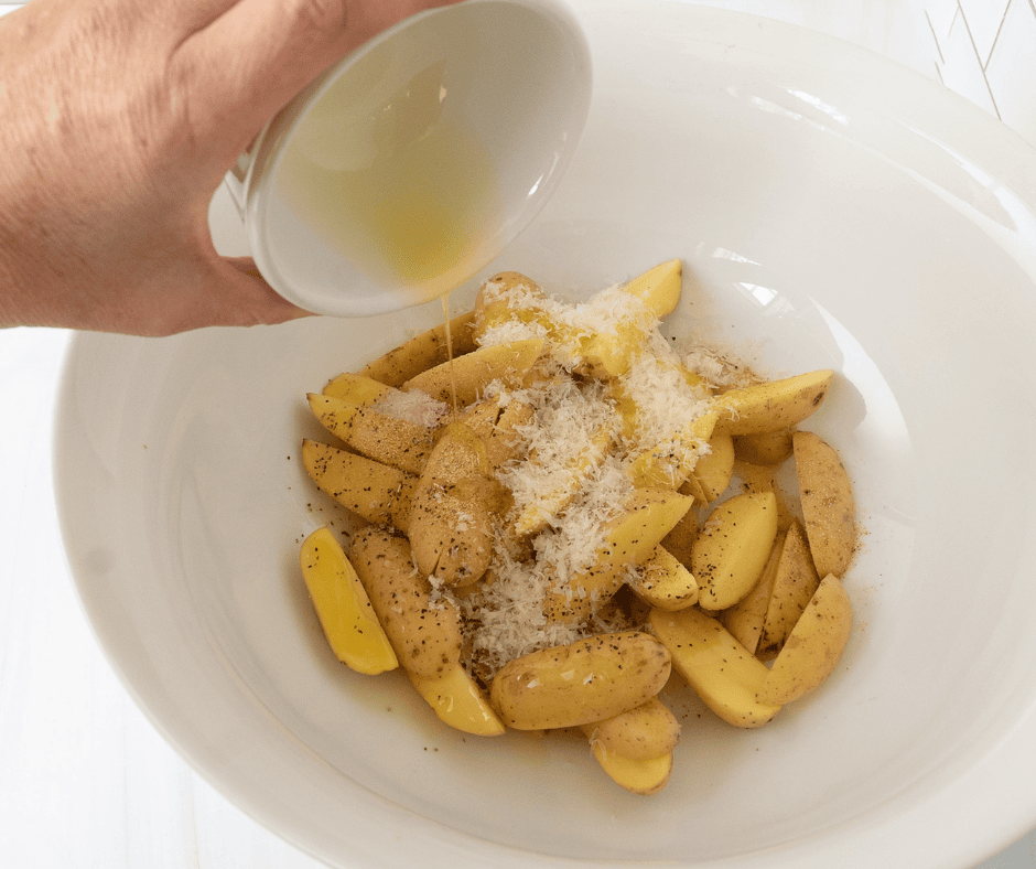 hand pouring olive oil on seasoned potatoes in a bowl