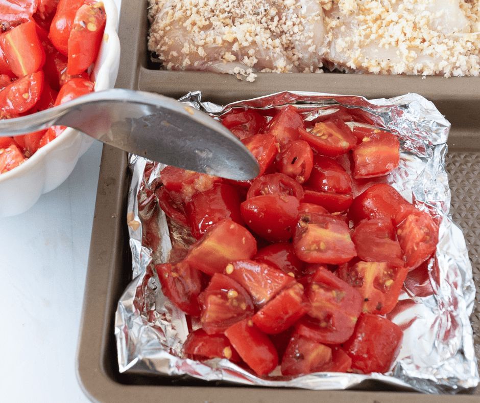 spoon adding tomato mixture to the aluminum foil bowl which sits on a sheet pan