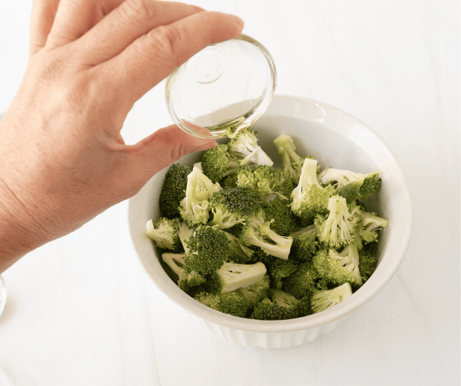 Hand pouring olive oil over seasoned broccoli