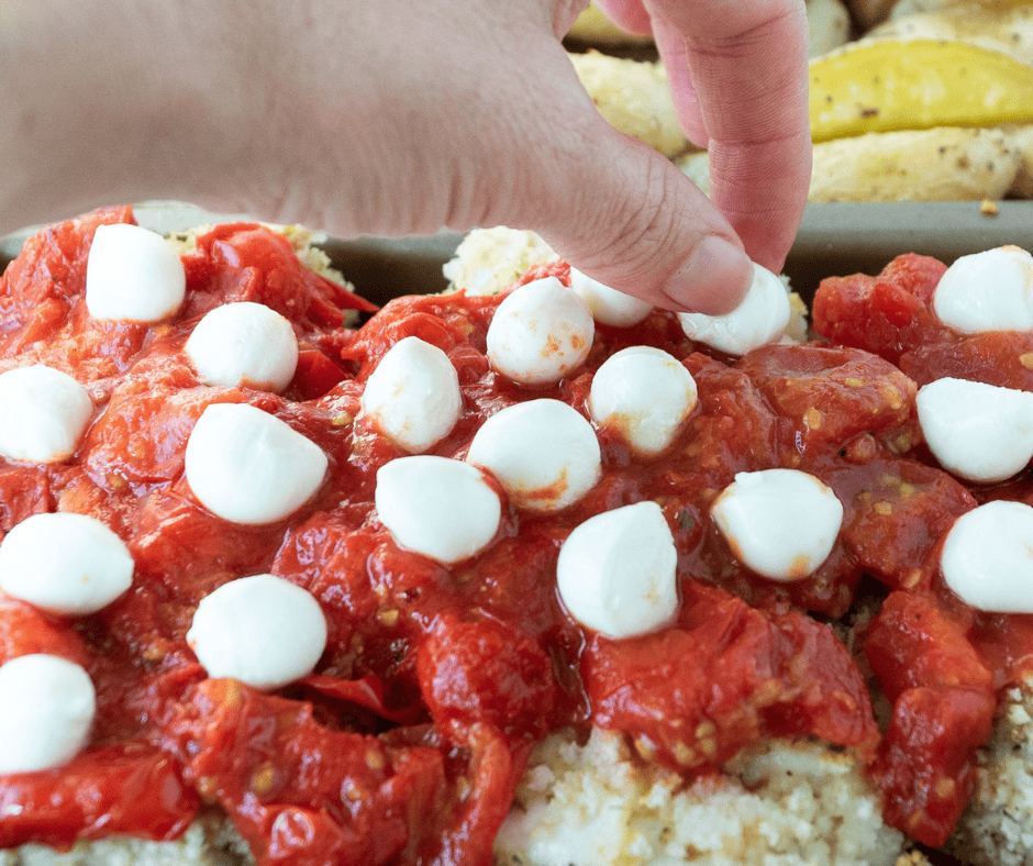 Dotting chicken with fresh mozzarella pearls for easy sheet pan chicken parmesan 