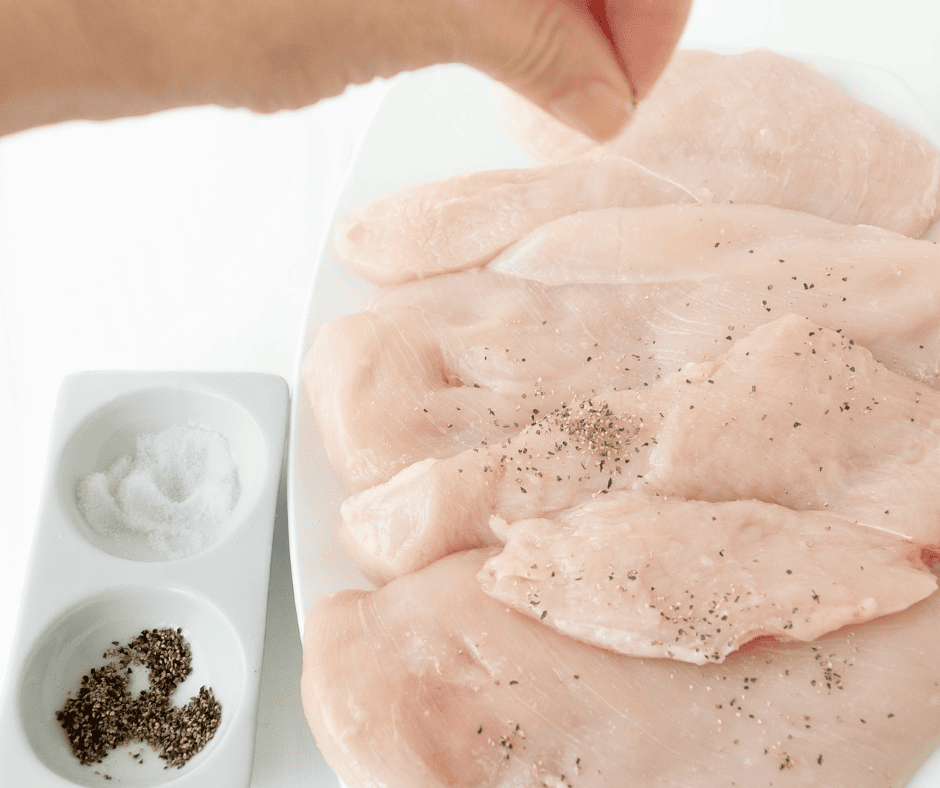 Hand sprinkling salt and pepper on chicken 