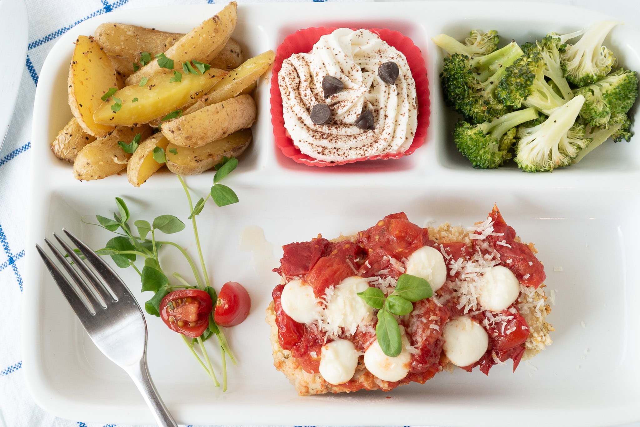 Easy Sheet Pan Chicken Parmesan Dinner Recipe Aerial Shot | A rectangular plate with chicken and sauce with cheese on it, broccoli, roasted potatoes and a dessert cube with a fork visible.