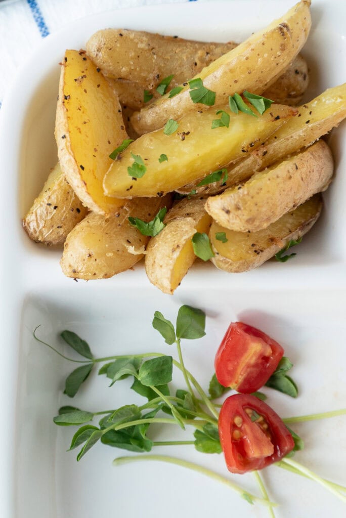 closet up of roasted fingerling potatoes with parsley. Sprigs of greens and halved grape tomatoes are visible. 