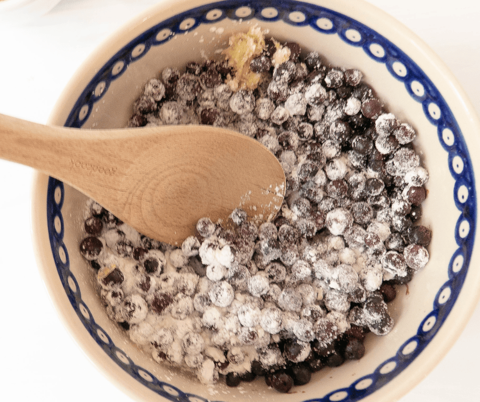 Process picture of blueberries in a bowl with a wooden spoon and flour