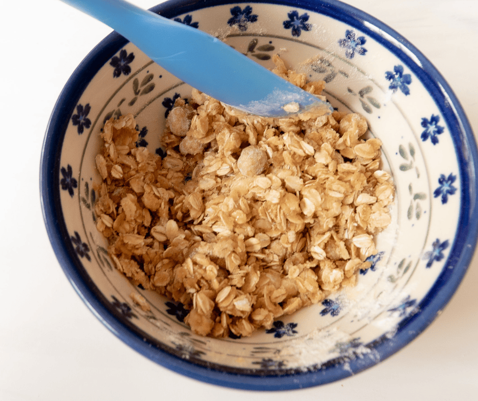 Process picture of crisp topping being mixed in a flowered bowl with a blue spatula.