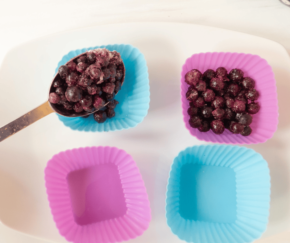 Process picture of a spoon putting blueberry mixture into silicone cups