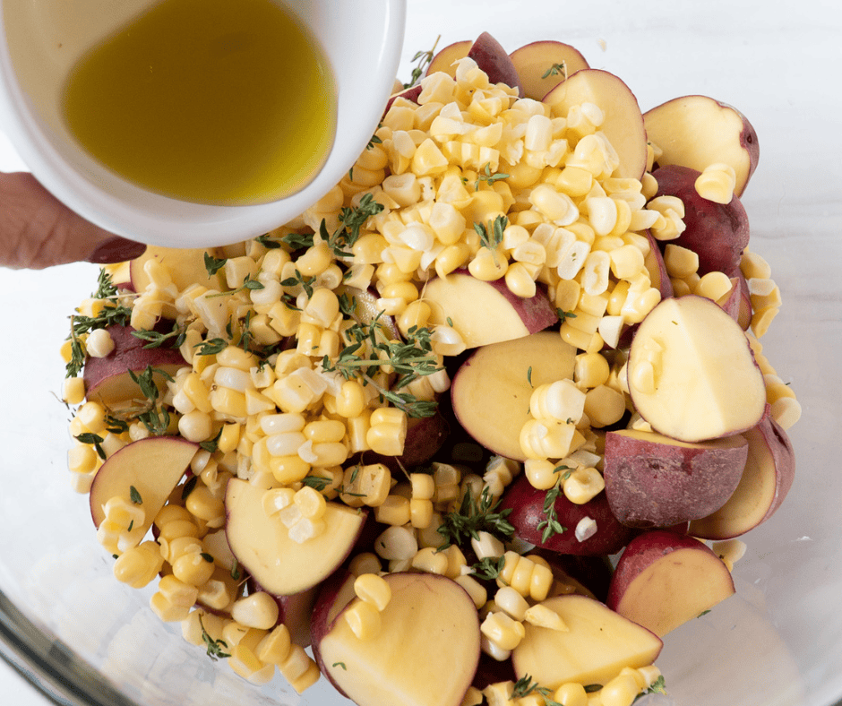 Process picture of dressing being poured on potatoes and corn