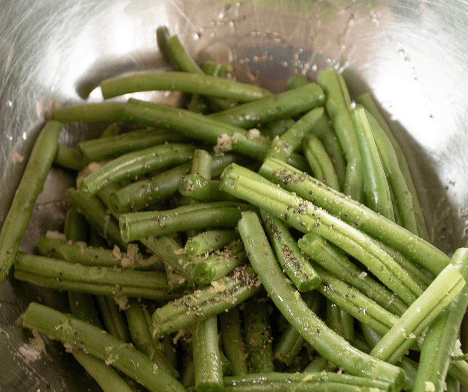 Process picture of green beans trimmed in a bowl with seasoning.