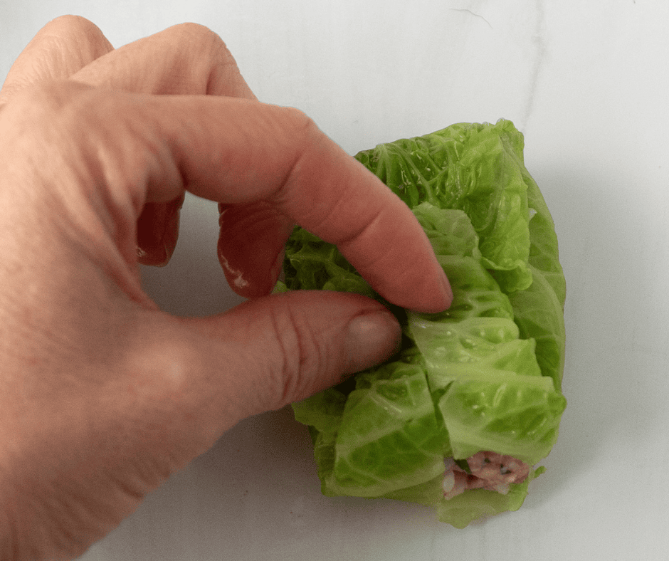 hand doing second fold of cabbage leaf.