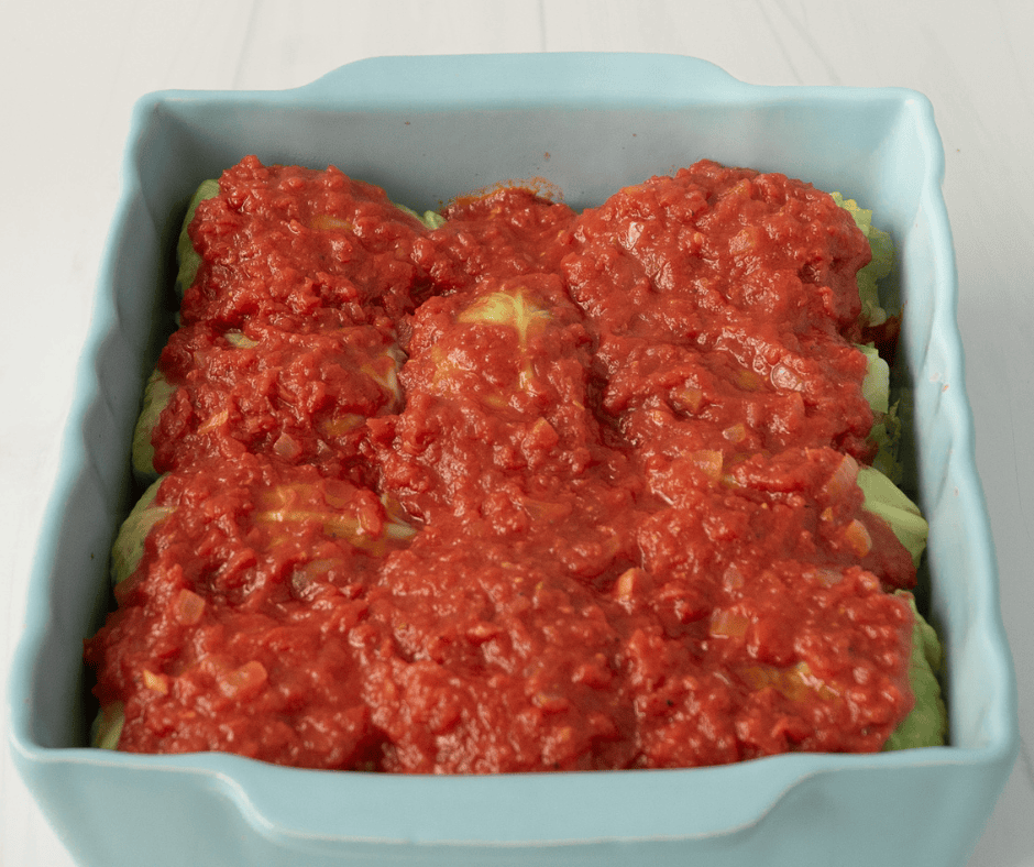 Red sauce covered stuffed cabbage rolls in a light blue square baking pan.