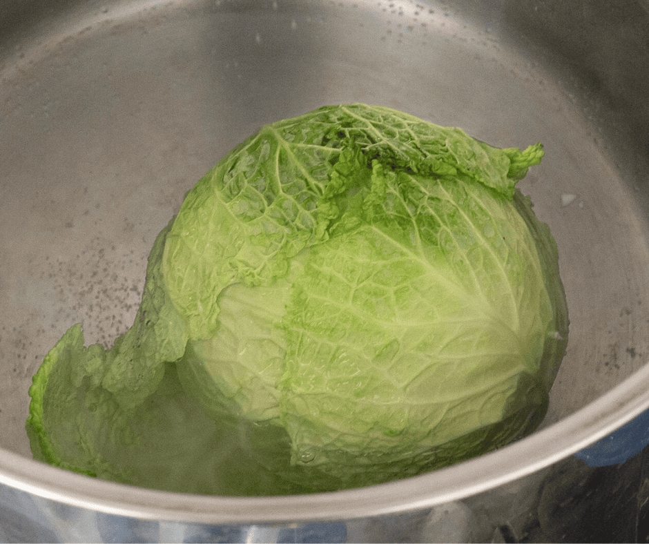 Submerging a whole head of cabbage in a boiling pot of salted water.
