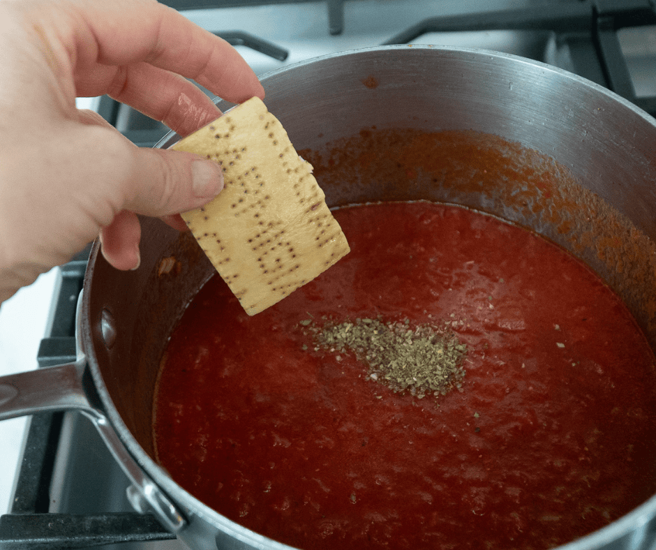 hand adding a parmesan cheese rind into a pot of simmering red sauce.