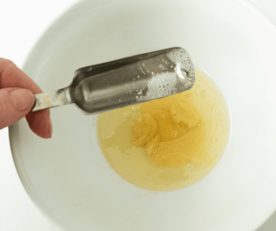Hand pouring a tablespoon of bubbling Prosecco into salad dressing ingredients bowl. 